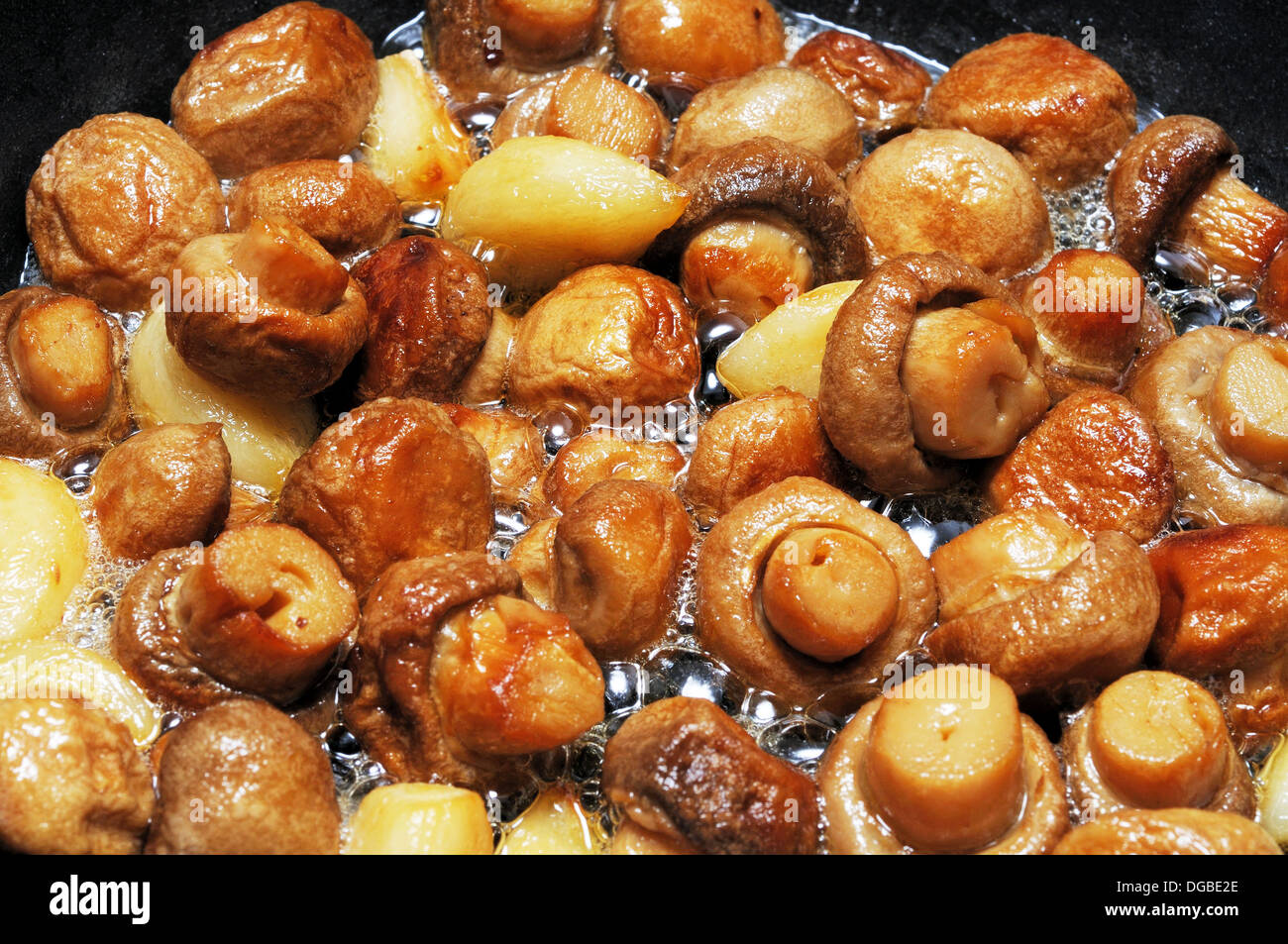 Whole button mushrooms and garlic cloves frying in butter Stock Photo