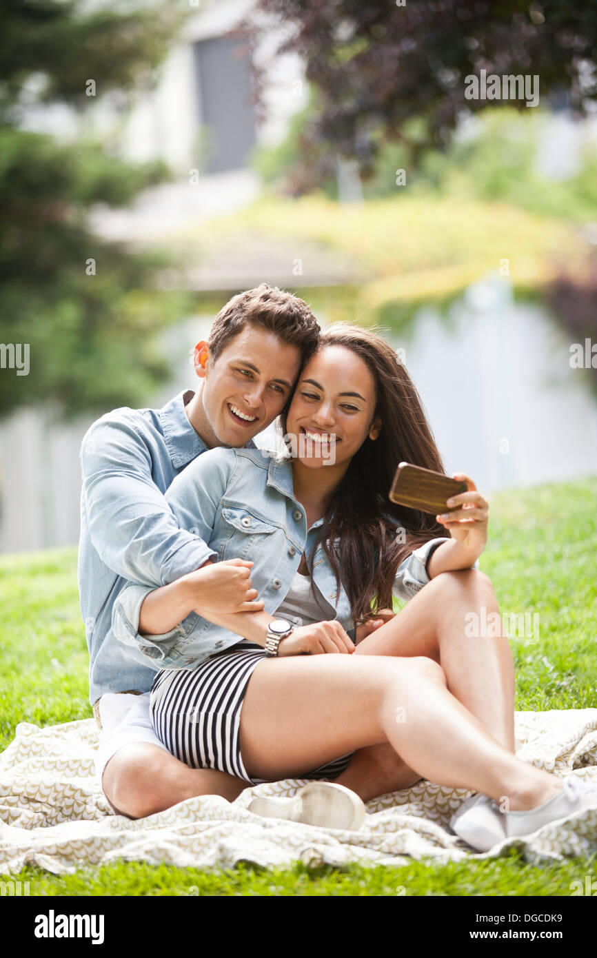 Young couple taking self portrait on camera phone in park, smiling Stock Photo