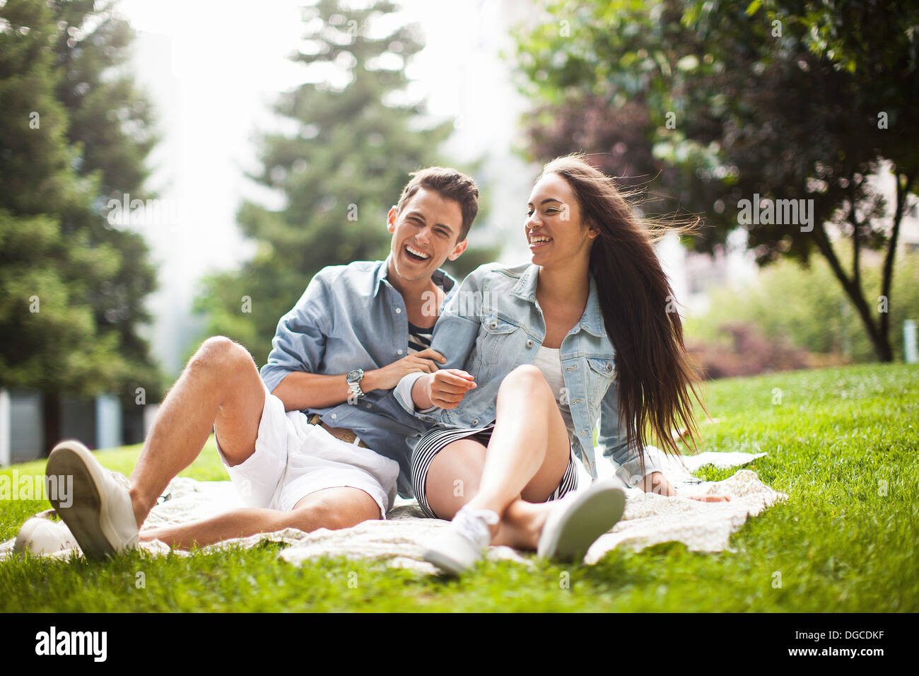 Young couple sitting in park, laughing Stock Photo