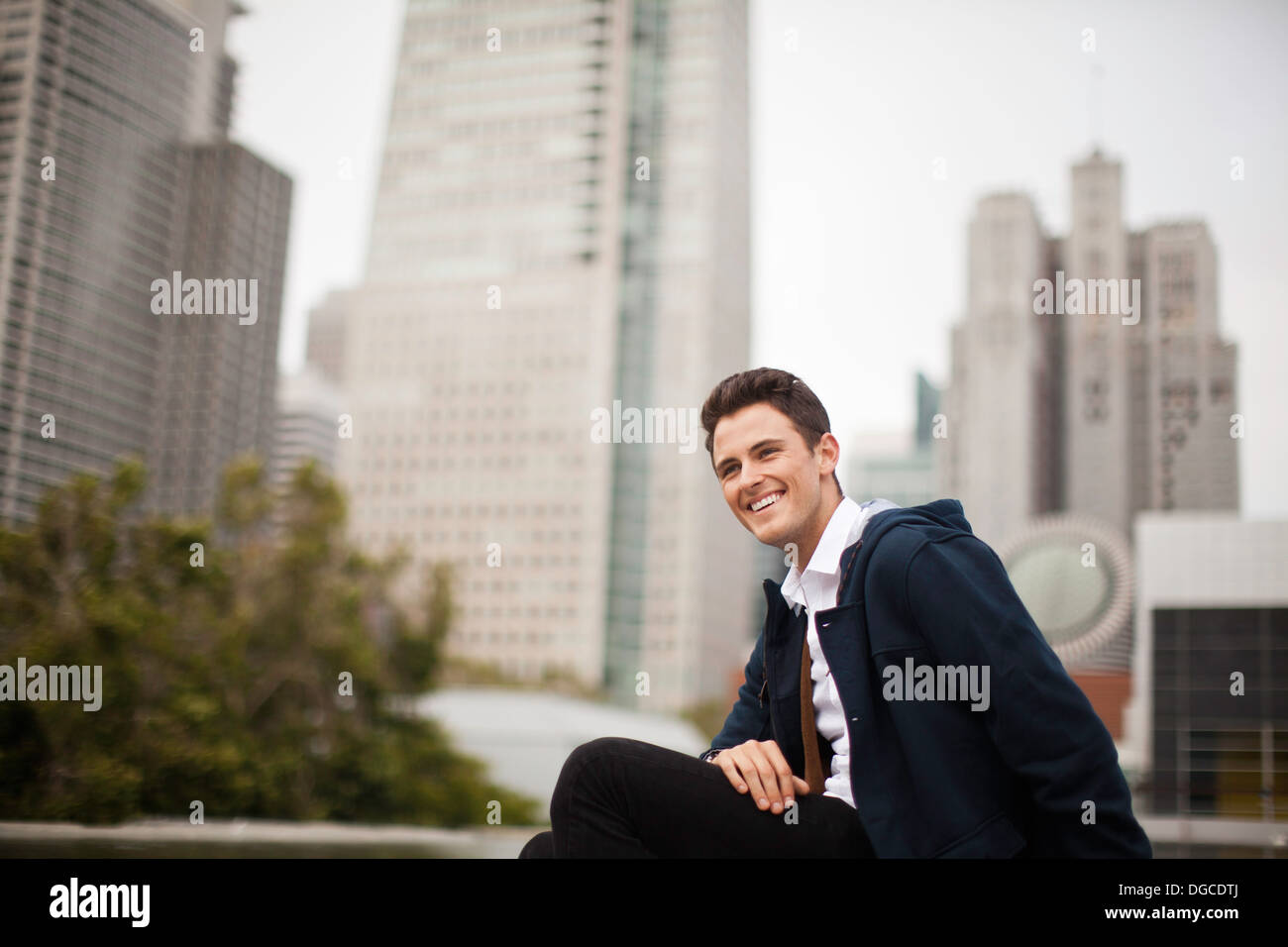 Young man sitting and smiling in city Stock Photo