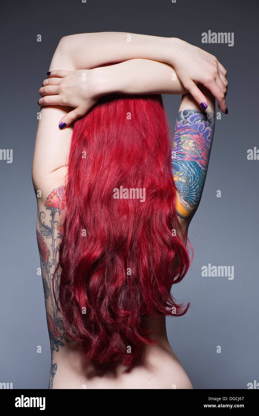 Young woman with long red hair and tattoos, studio shot Stock Photo