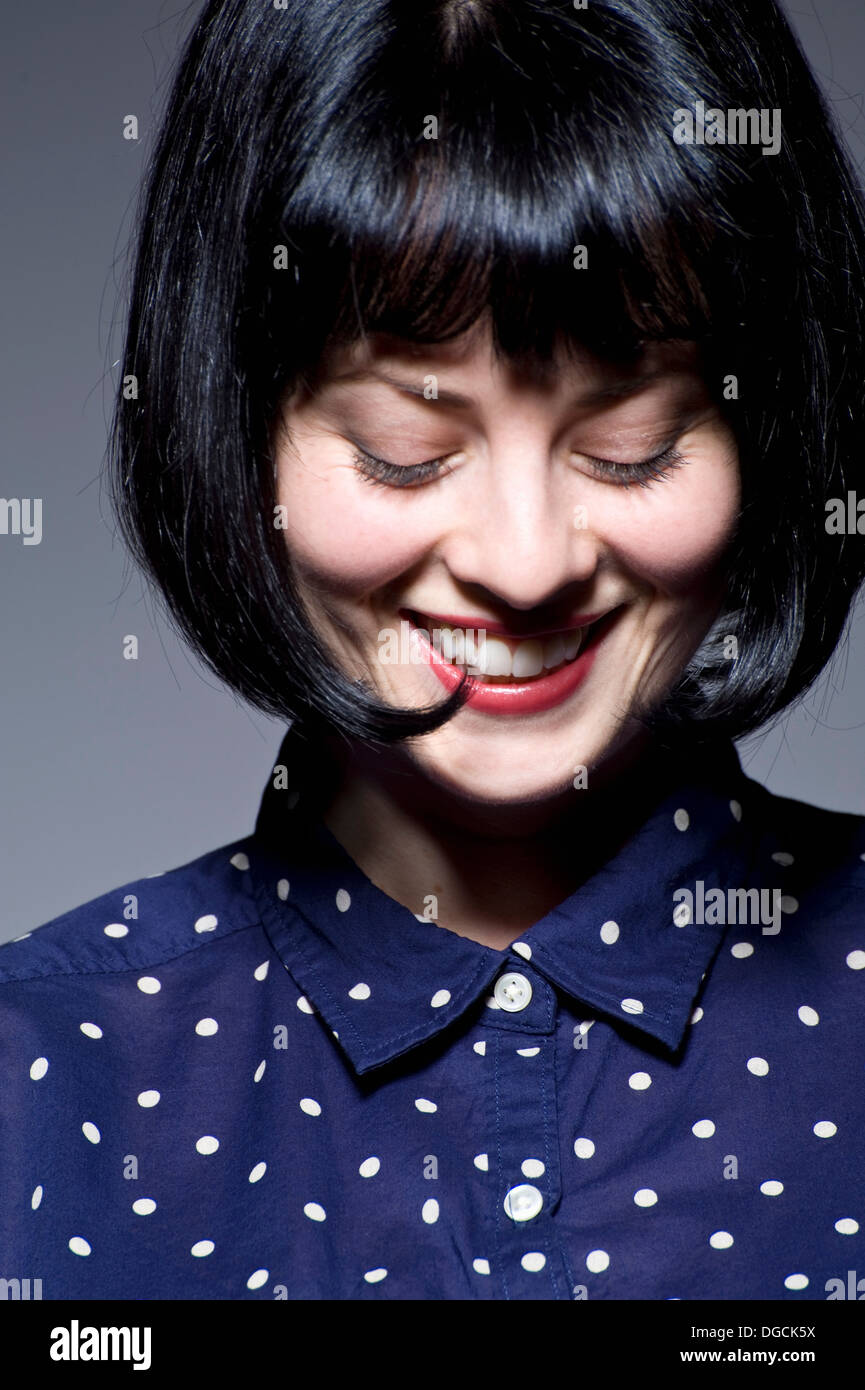 Young woman in blue spotted blouse looking down, smiling Stock Photo