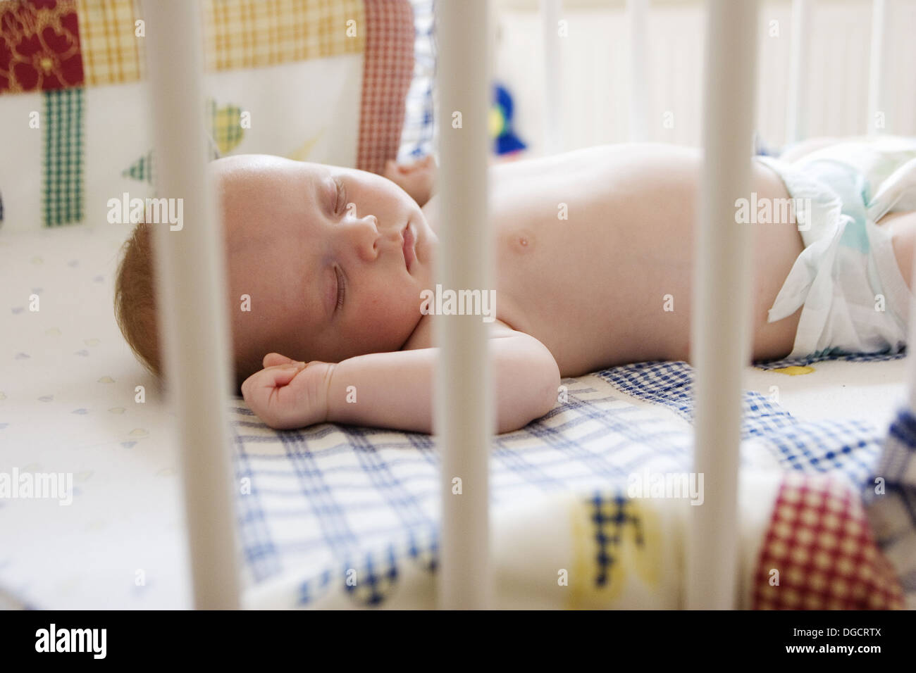 Eight week old baby lying sleeping in his cot, wearing just a nappy