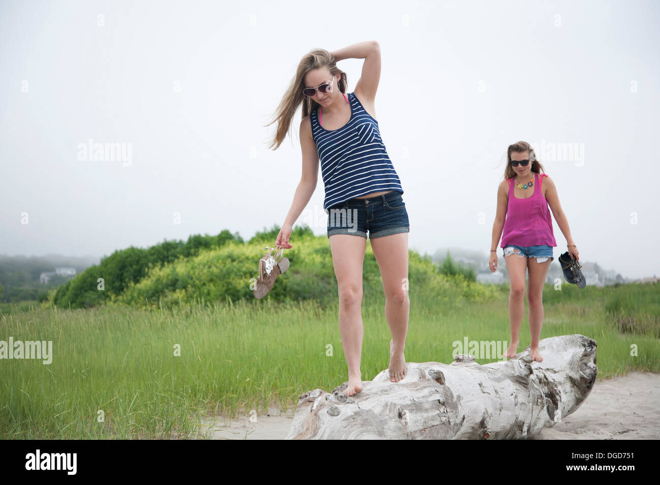 Young women walking along log on beach Stock Photo