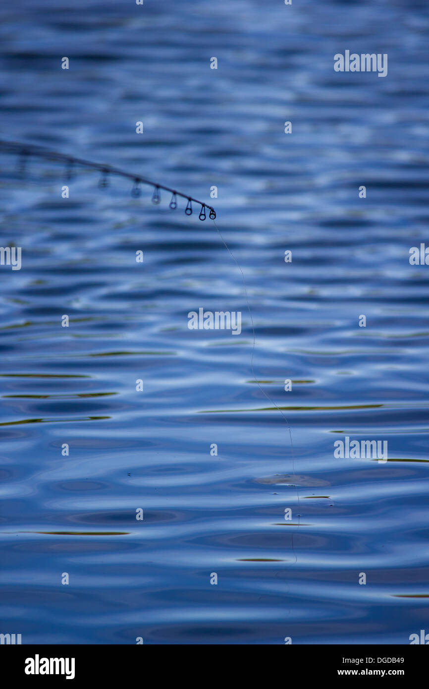 The tip of a fishing rod waits to strike. The surface of the lake is windswept Stock Photo