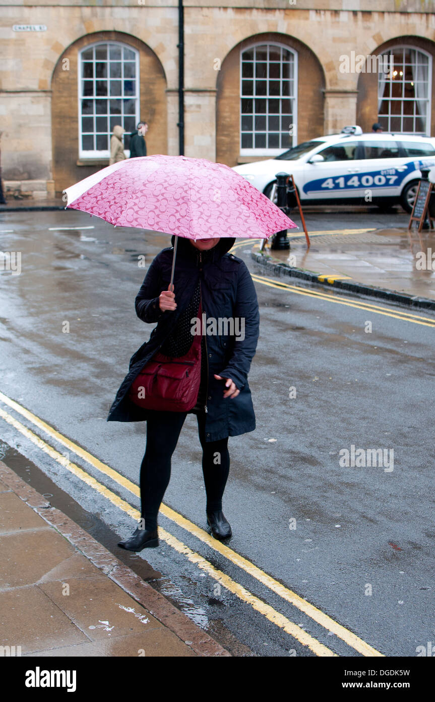 Woman carrying umbrella stepping up kerb, Stratford-upon-Avon, UK Stock Photo