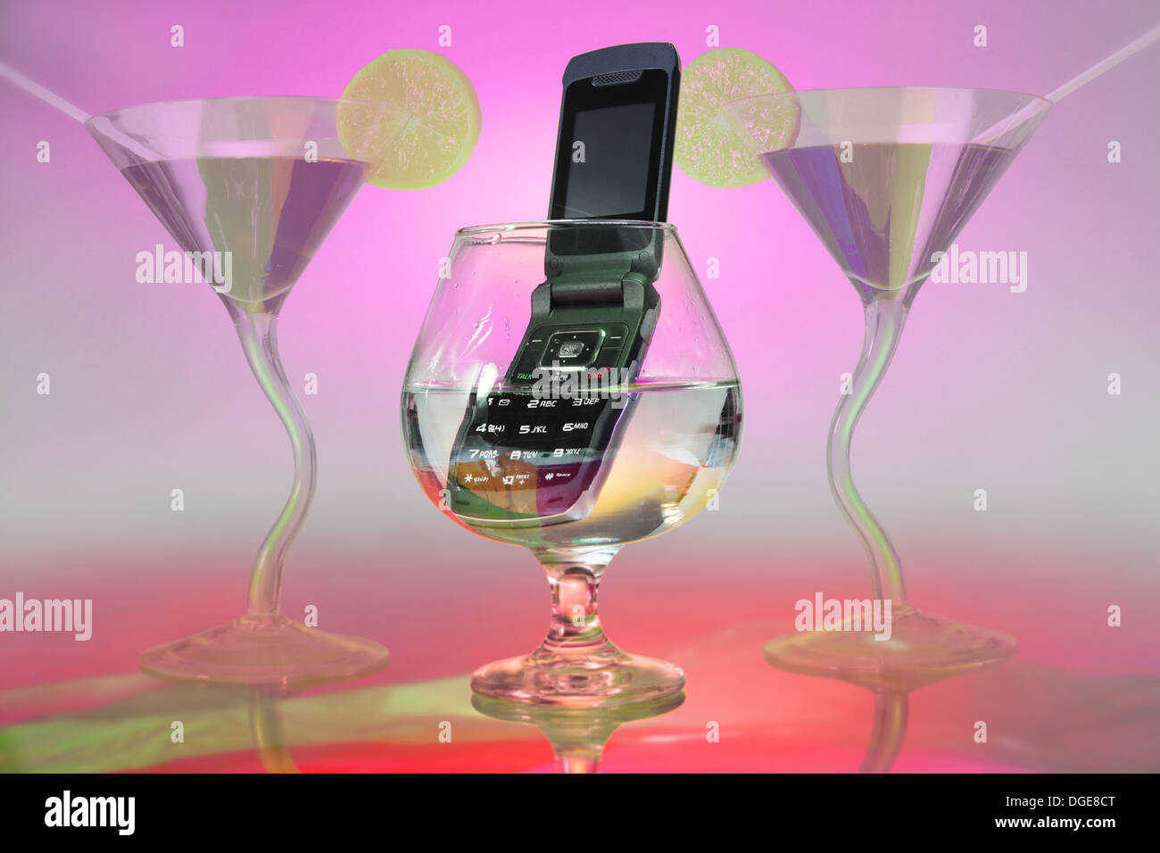 In the middle, you see a brandy glass in which a cell phone is immersed. two cocktail glasses frame the scene Stock Photo