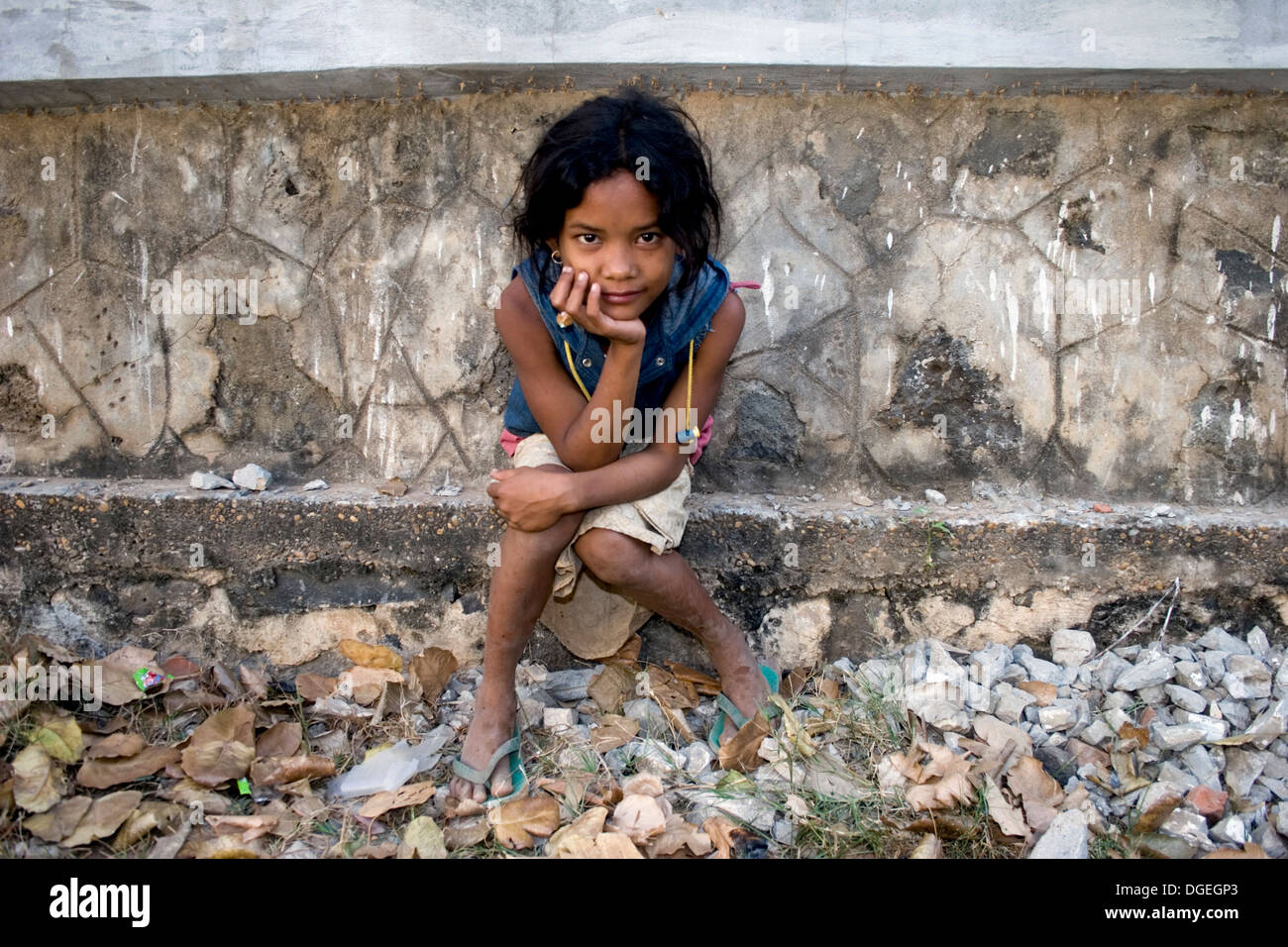 A young girl living in poverty is relaxing on a Buddhist stupa in Kampong Cham, Cambodia. Stock Photo