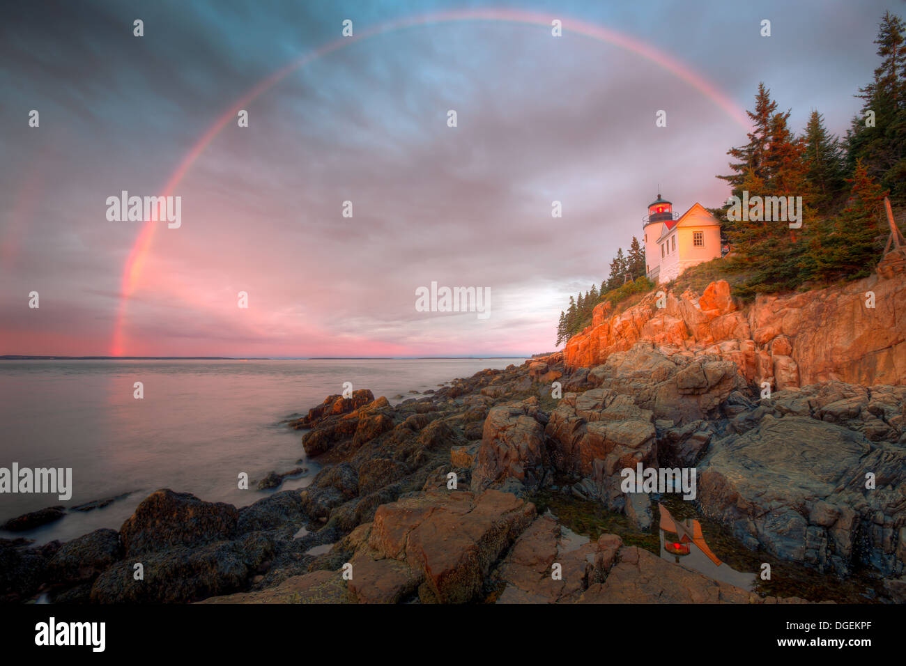 A double rainbow appears briefly at sunrise over Bass Harbor Head Lighthouse, and is reflected in a tidal pool, in Acadia National Park. Stock Photo