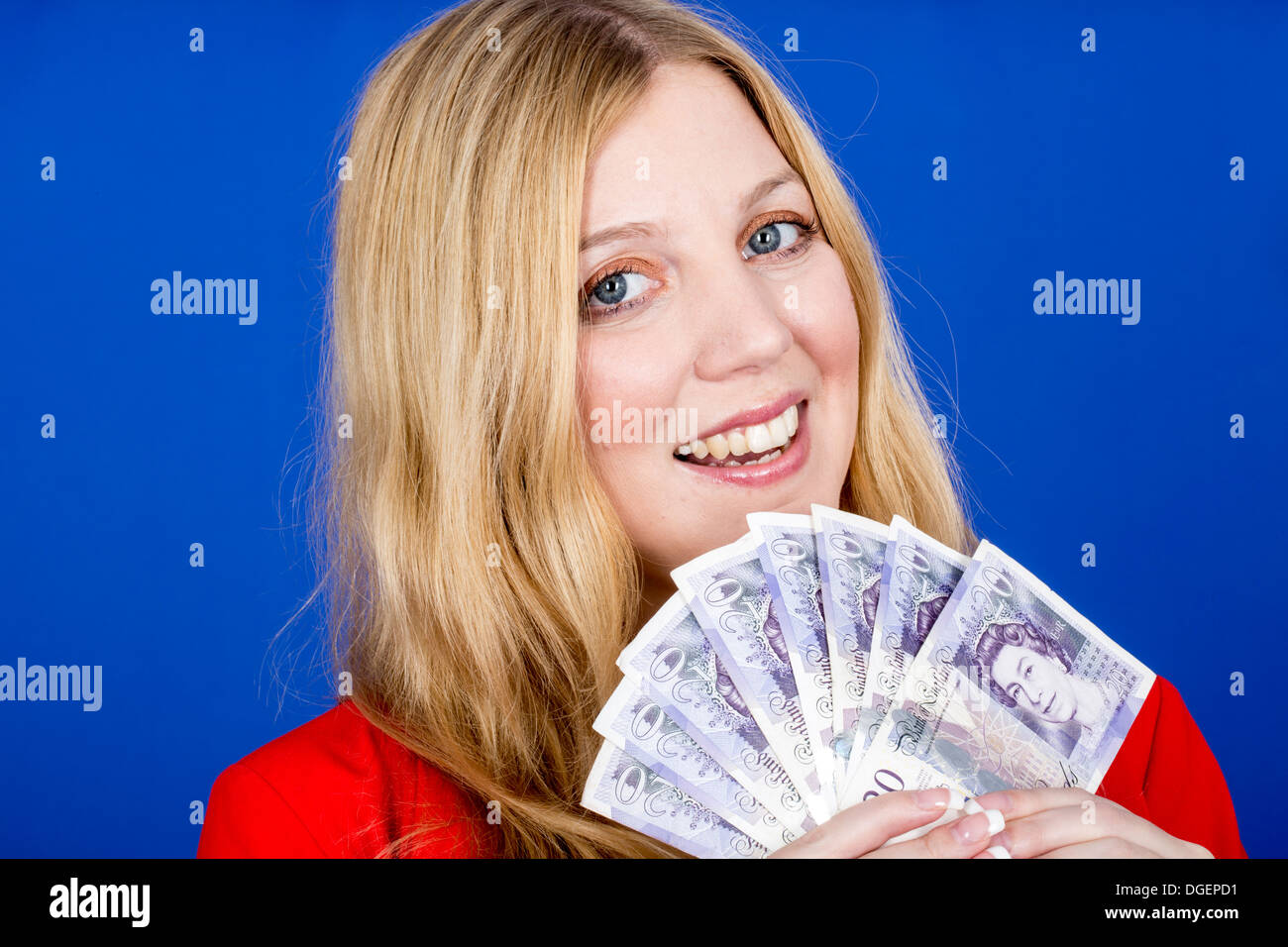 Young Happy Successful Blonde Caucasian Business Woman Holding A Fan Of British Banknotes Money, Alone And Isolated Against A Blue Background Stock Photo