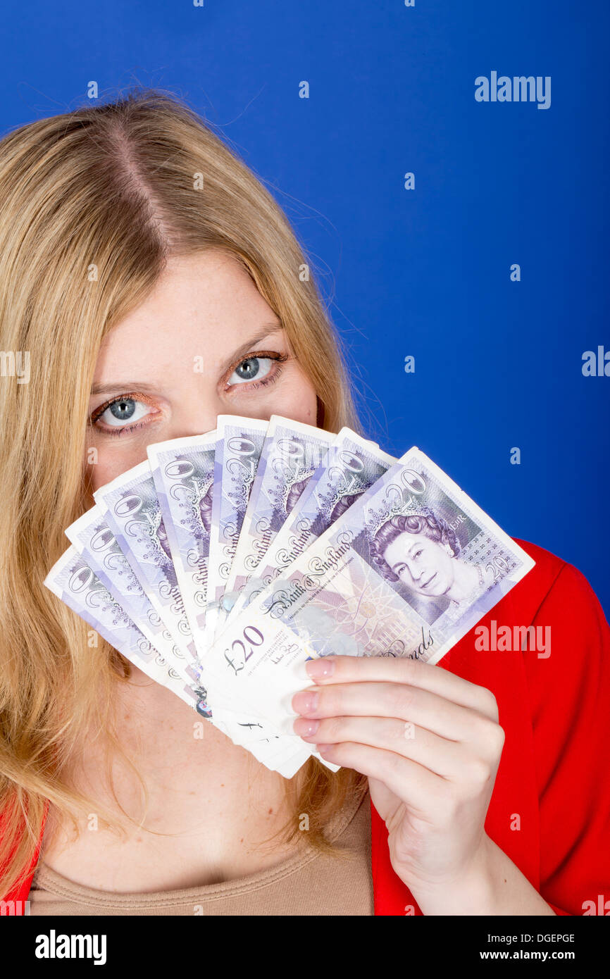 Young Happy Successful Blonde Caucasian Business Woman Holding A Fan Of British Banknotes Money, Alone And Isolated Against A Blue Background Stock Photo