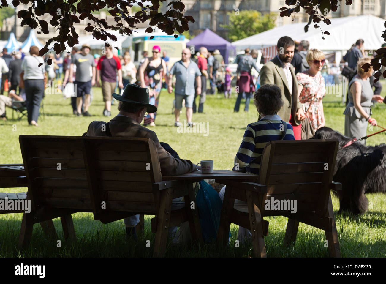 Couple taking break having drink in shade visitors walk around hot sunny Game Country Fair 2013 Burghley House Stamford England Stock Photo