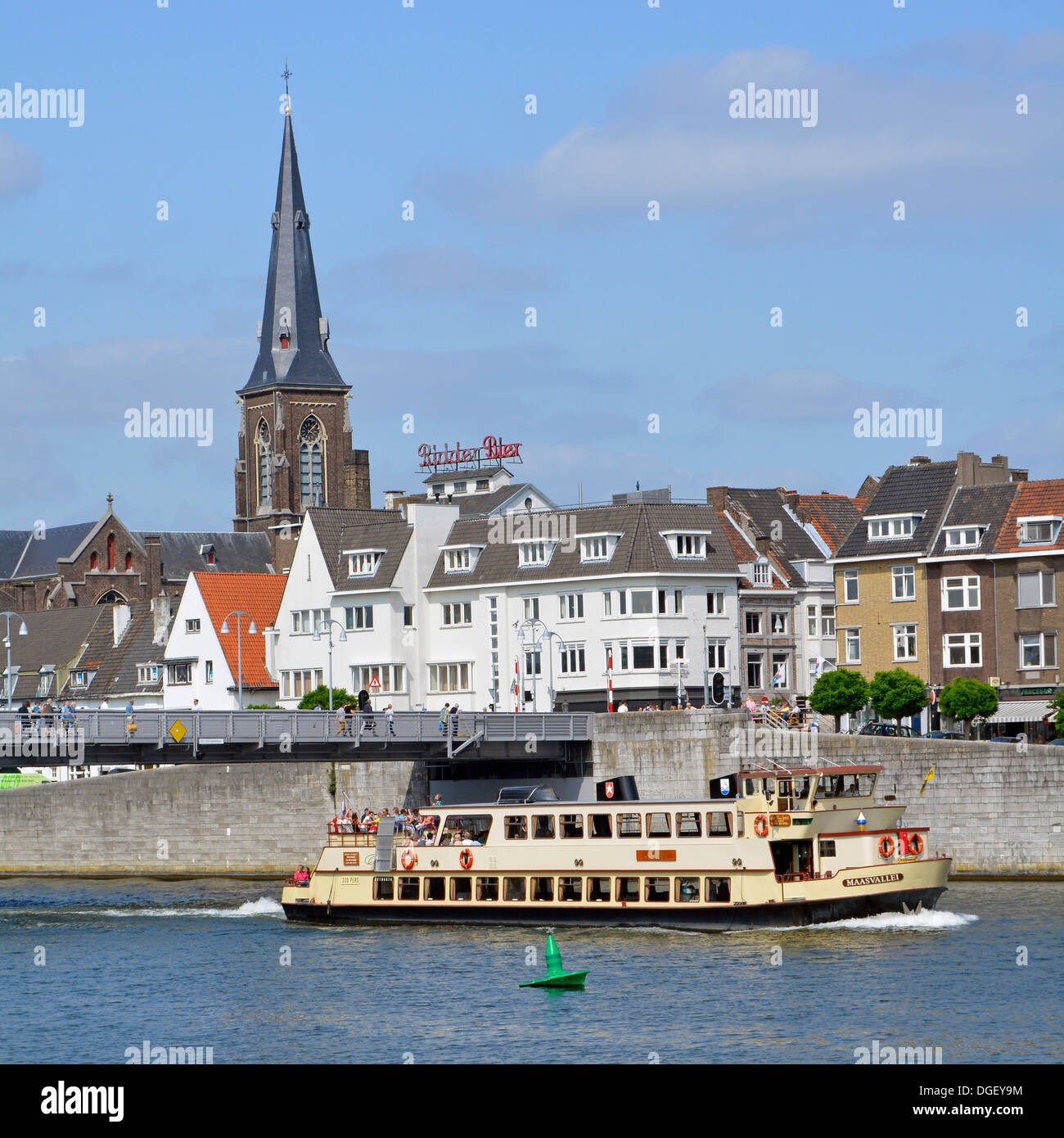 A tourist boat cruising on the Meuse River in Maastricht, with passengers enjoying the view of the city's historic buildings and waterfront on a sunny day.