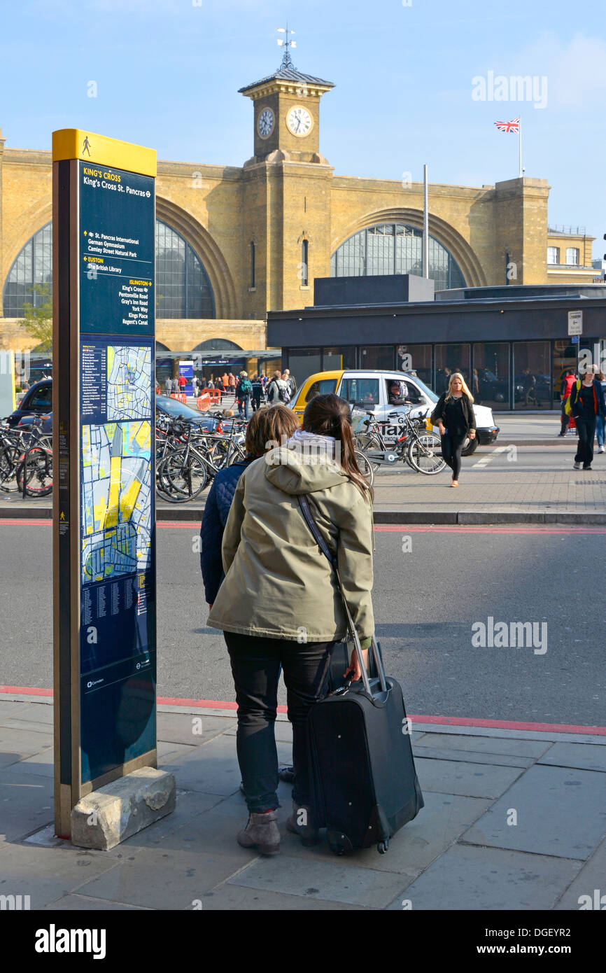 Travelers beside legible London street sign with refurbished Kings Cross railway train station beyond Stock Photo