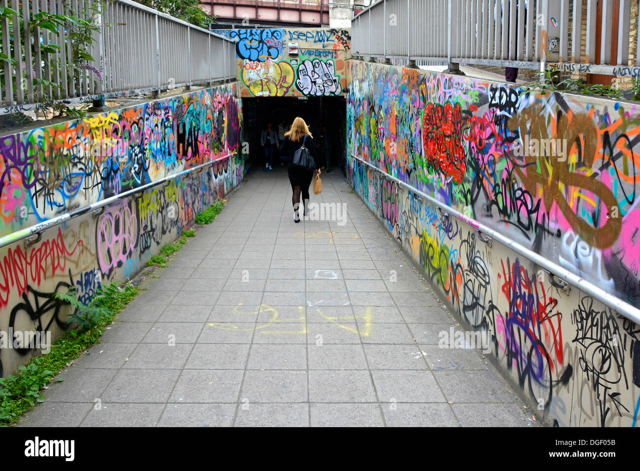 Graffiti covered walls and lone young woman walking towards the unknown into dark subway tunnel near Waterloo station London England UK Stock Photo