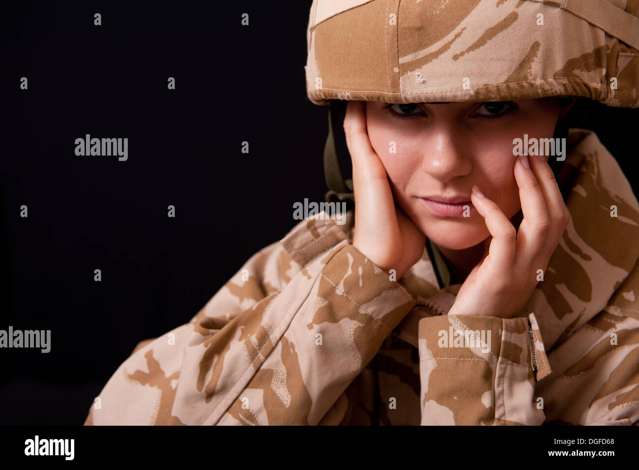 Distraught young female soldier wearing British Military uniform against a black background. Stock Photo