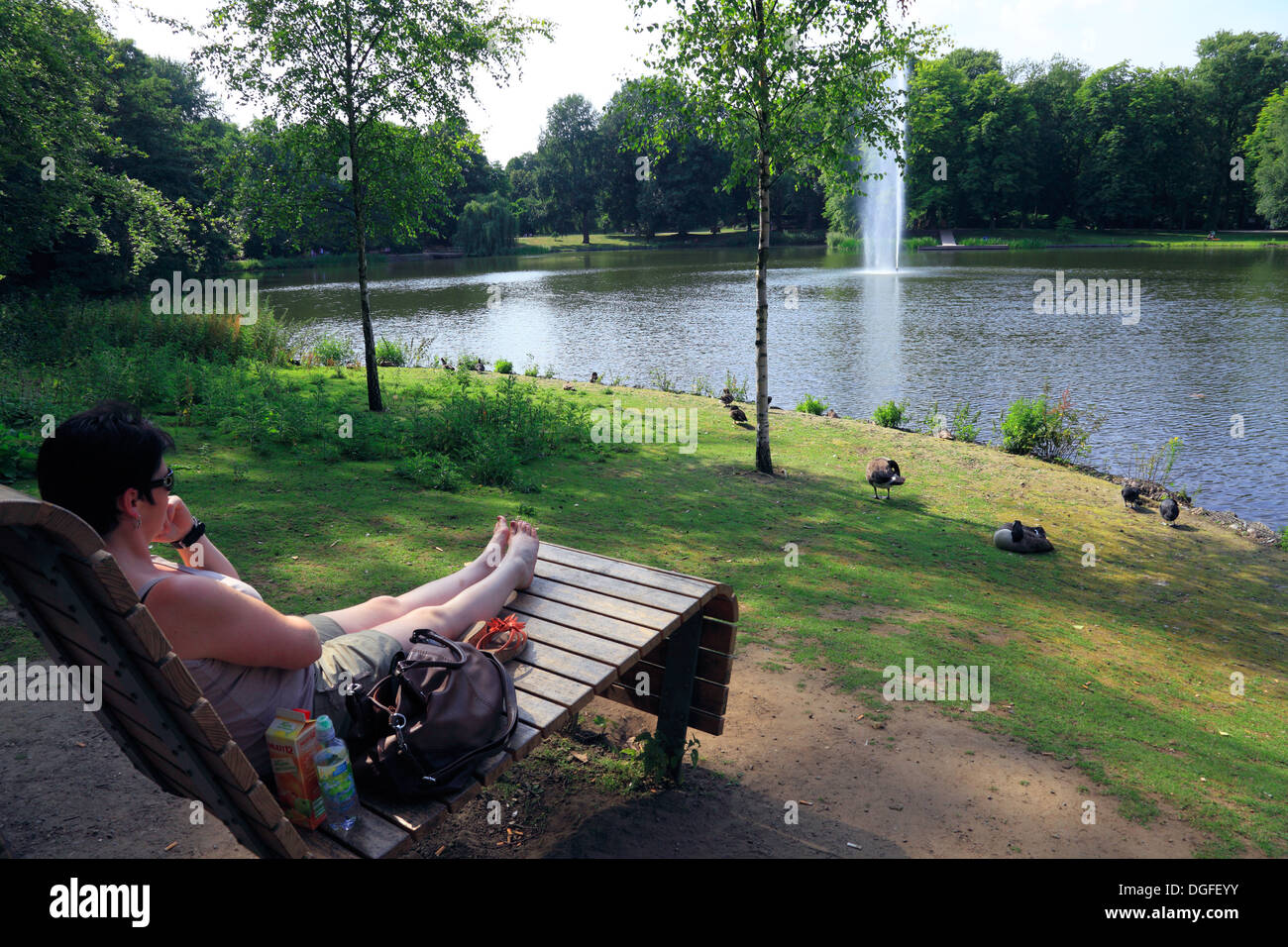 Frau sitzt auf einer Parkbank im Kaisergarten, dahinter ein Teich mit