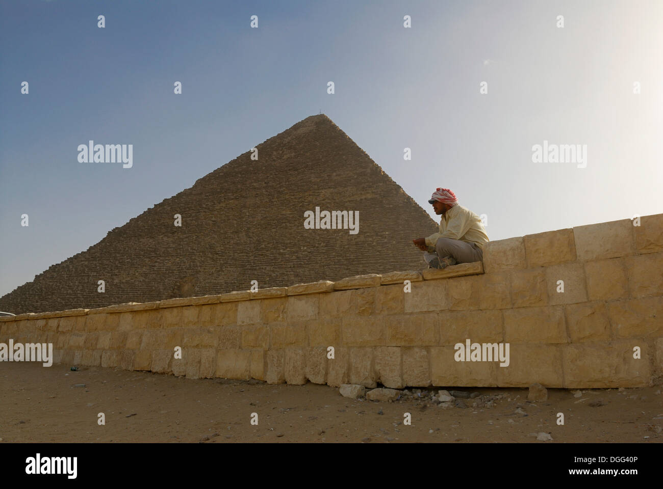 Egyptian man sitting on wall in front of the Cheops Pyramid, Giza Pyramids, Cairo, Egypt, Africa Stock Photo