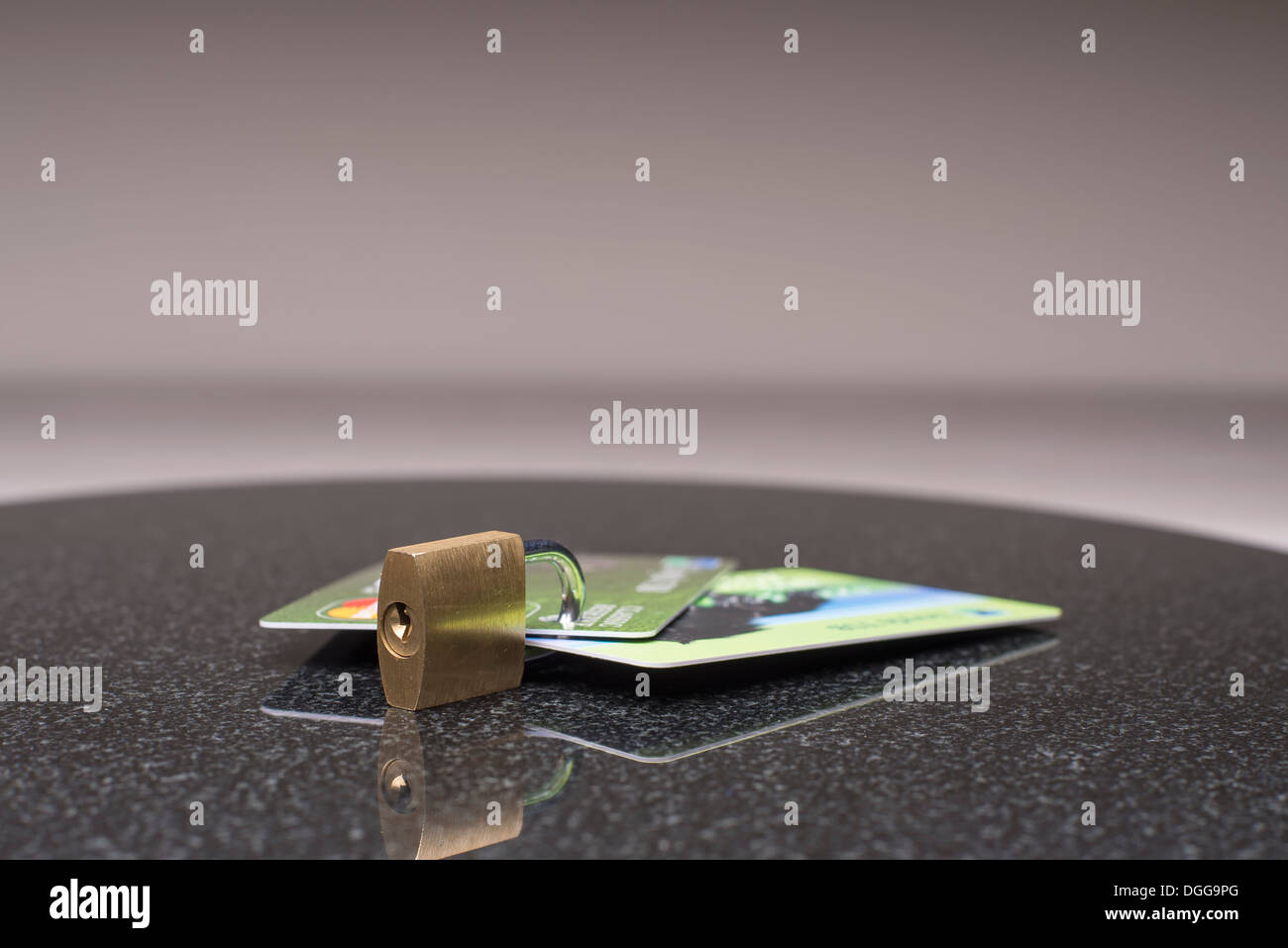 concept showing a padlock going through and locking bank credit cards  to show they are secured safe shot on a reflective table Stock Photo