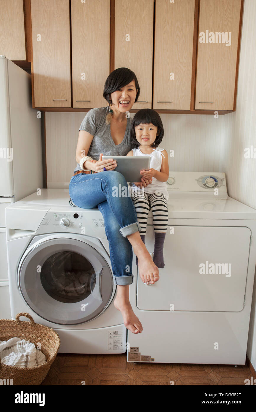 Mother and daughter sitting on washing machine using tablet Stock Photo