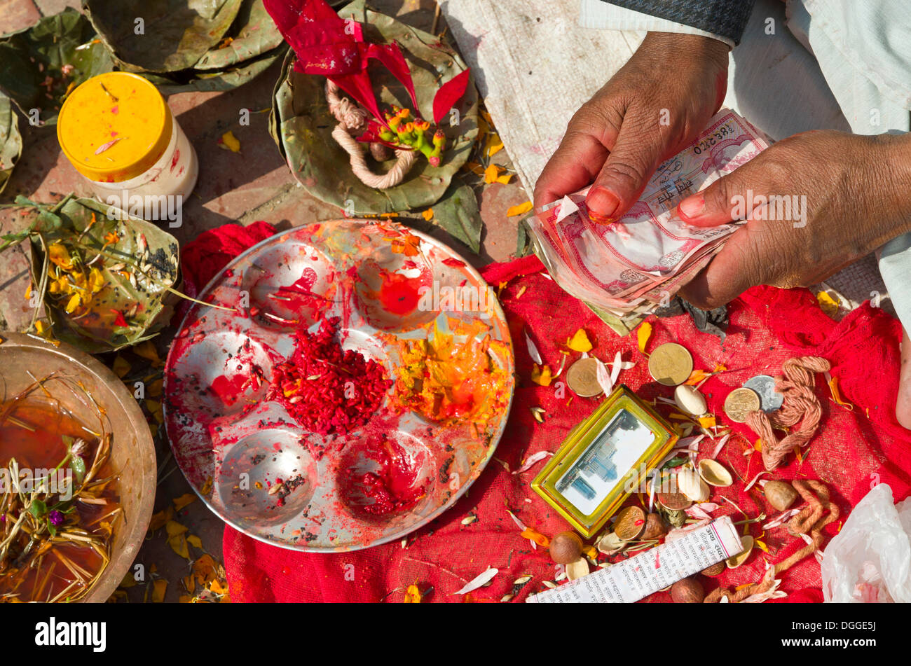 Shell cone, bell, colourpowder and other small items to work with as a priest, hands holding some notes, Kathmandu Stock Photo