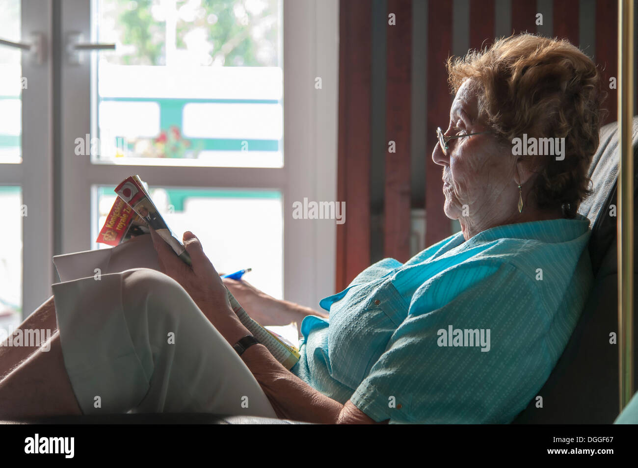 Elderly woman sitting in an armchair reading a newspaper, Grevenbroich ...