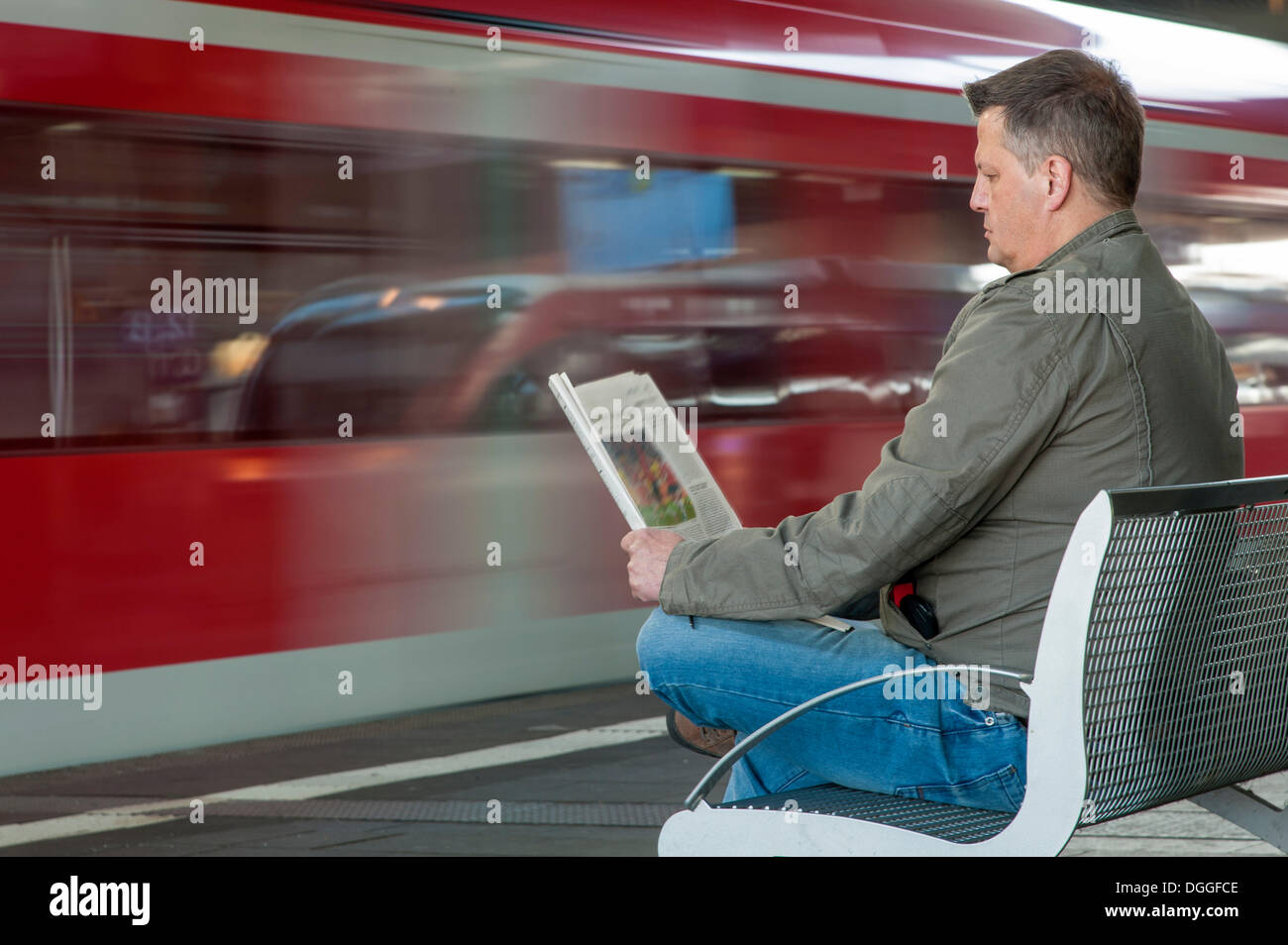 Man sitting on a bench at a station reading a newspaper, Duesseldorf, North Rhine-Westphalia Stock Photo