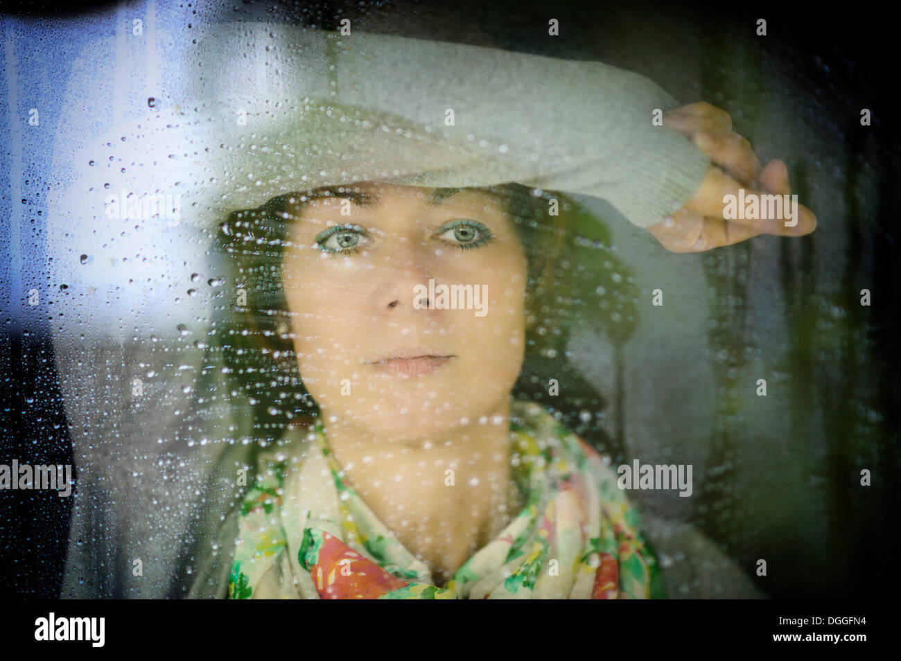 Young woman looking through a window on a rainy day, Grevenbroich, Rhineland, North Rhine-Westphalia, Germany Stock Photo