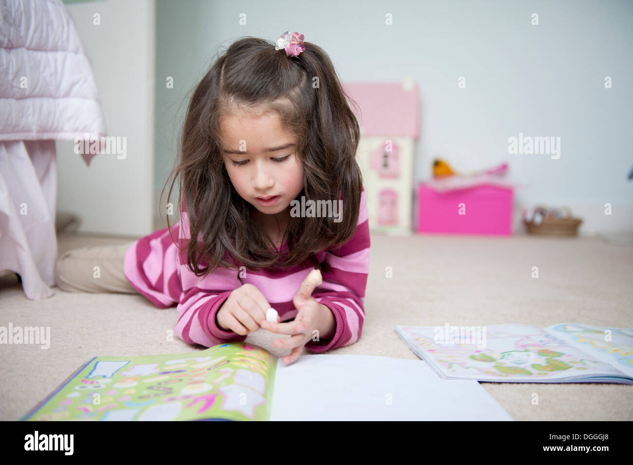 Girl lying on front and reading sticker book Stock Photo