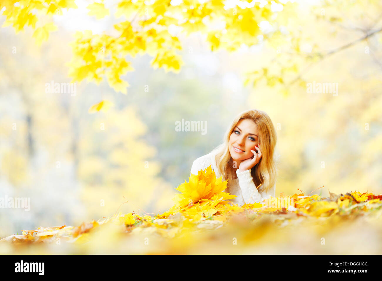 Young woman laying down on the ground covered dry autumnal foliage in beautiful park Stock Photo