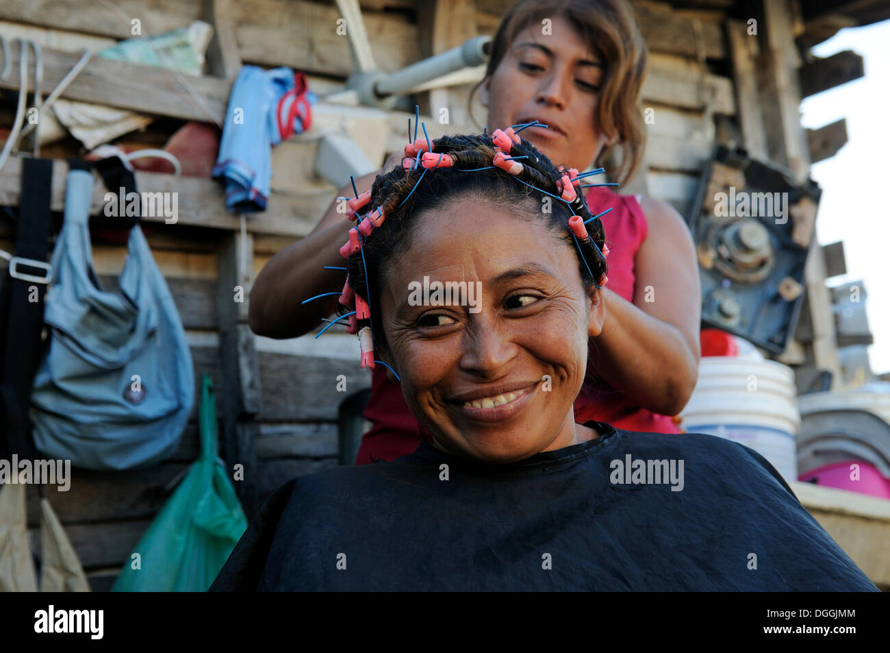 Woman doing another woman's hair in front of her hut, customer is 40 years old, in a poor neighborhood, Cancun Stock Photo