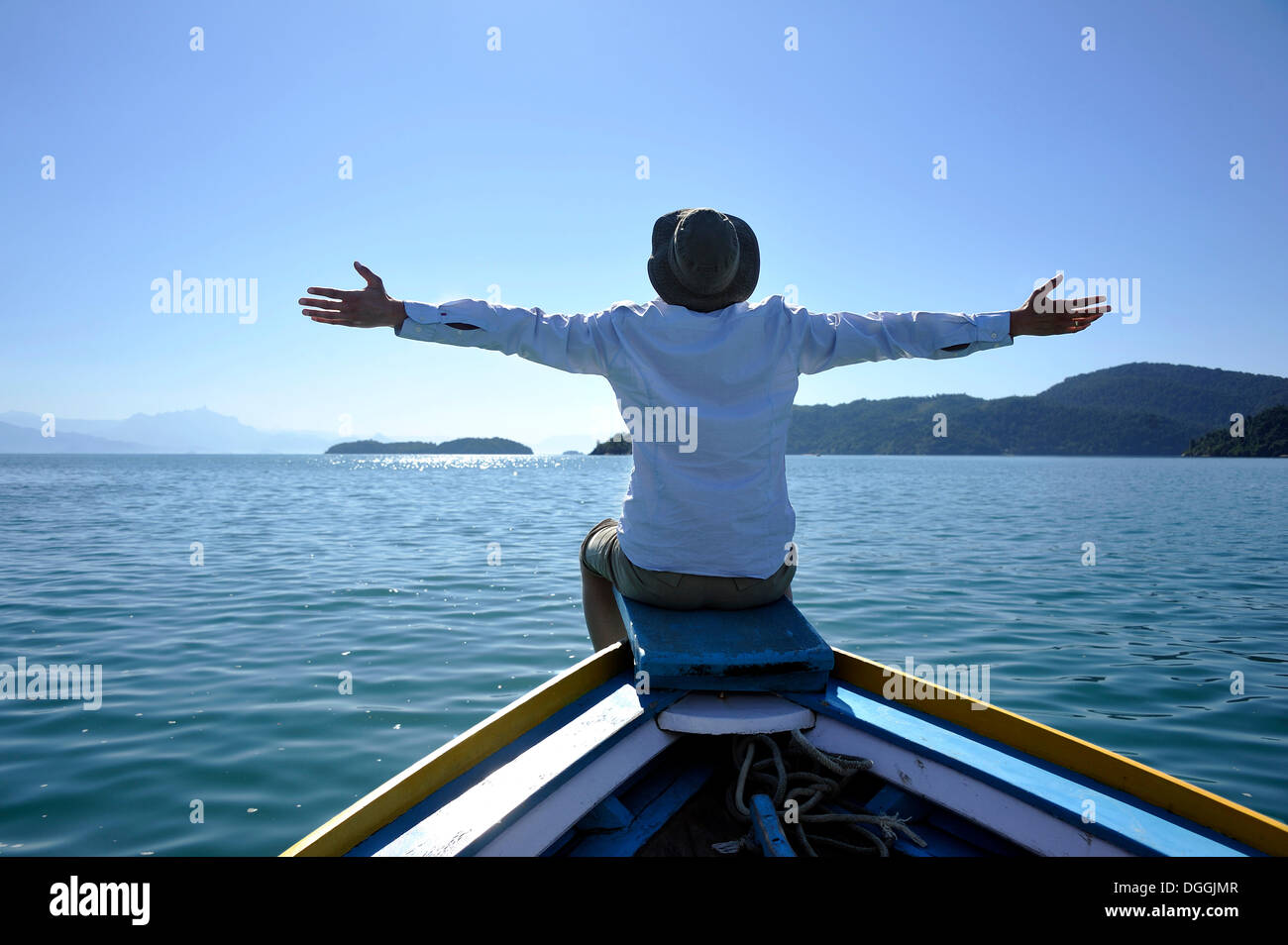 Young man sitting on the bow of a fishing boat with his arms wide open, Bay of Paraty or Parati, State of Rio de Janeiro, Brazil Stock Photo