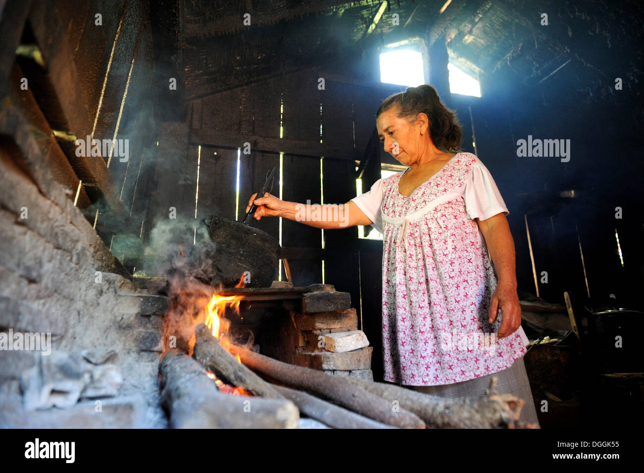Elderly woman in a basic kitchen cooking on an open fire, Carayao, Caaguazú Department, Paraguay Stock Photo