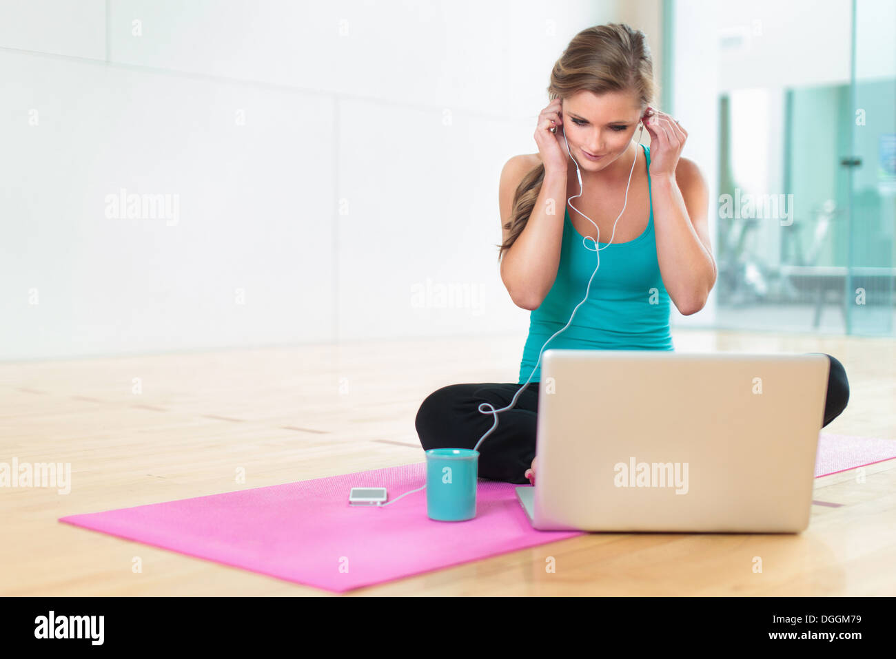 Young woman on yoga mat listening to smartphone Stock Photo