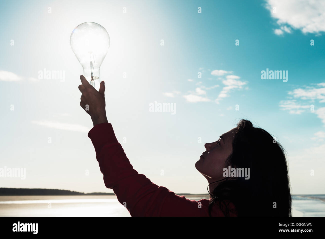 Woman holding light bulb in sky Stock Photo
