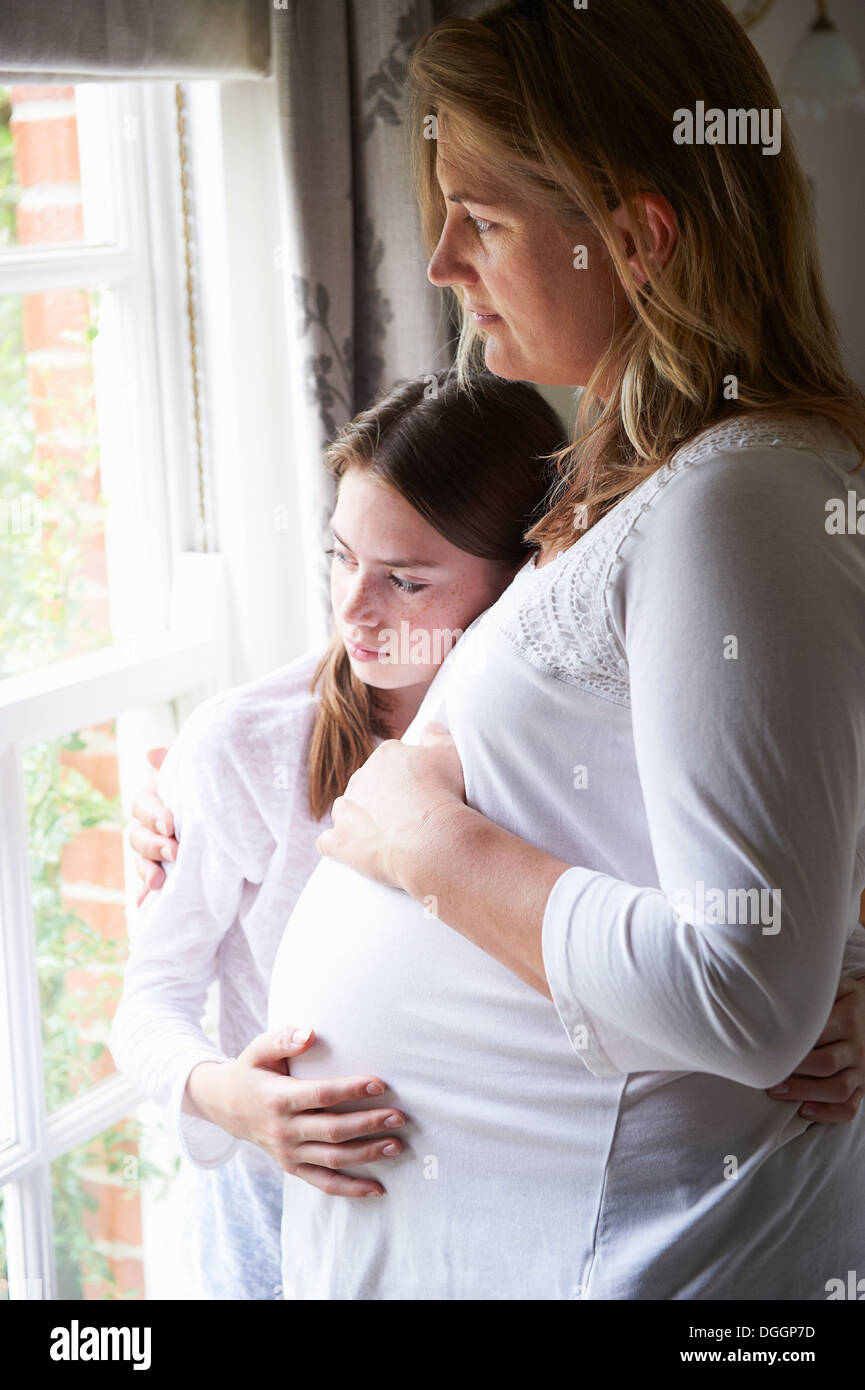 Pregnant mother with teenage daughter looking through window Stock Photo