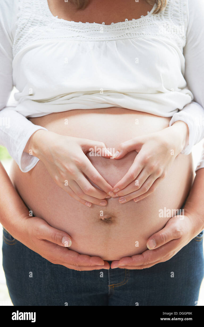 Hands in heart shape on pregnant woman's stomach Stock Photo