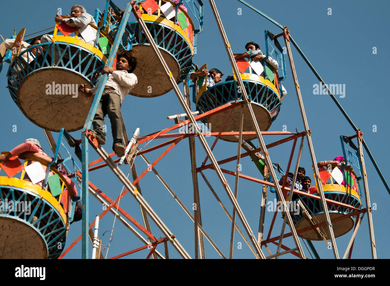 Young Indian ferris wheel operator hanging outside of the wheel. Taken in Jaisalmer desert festival. Stock Photo