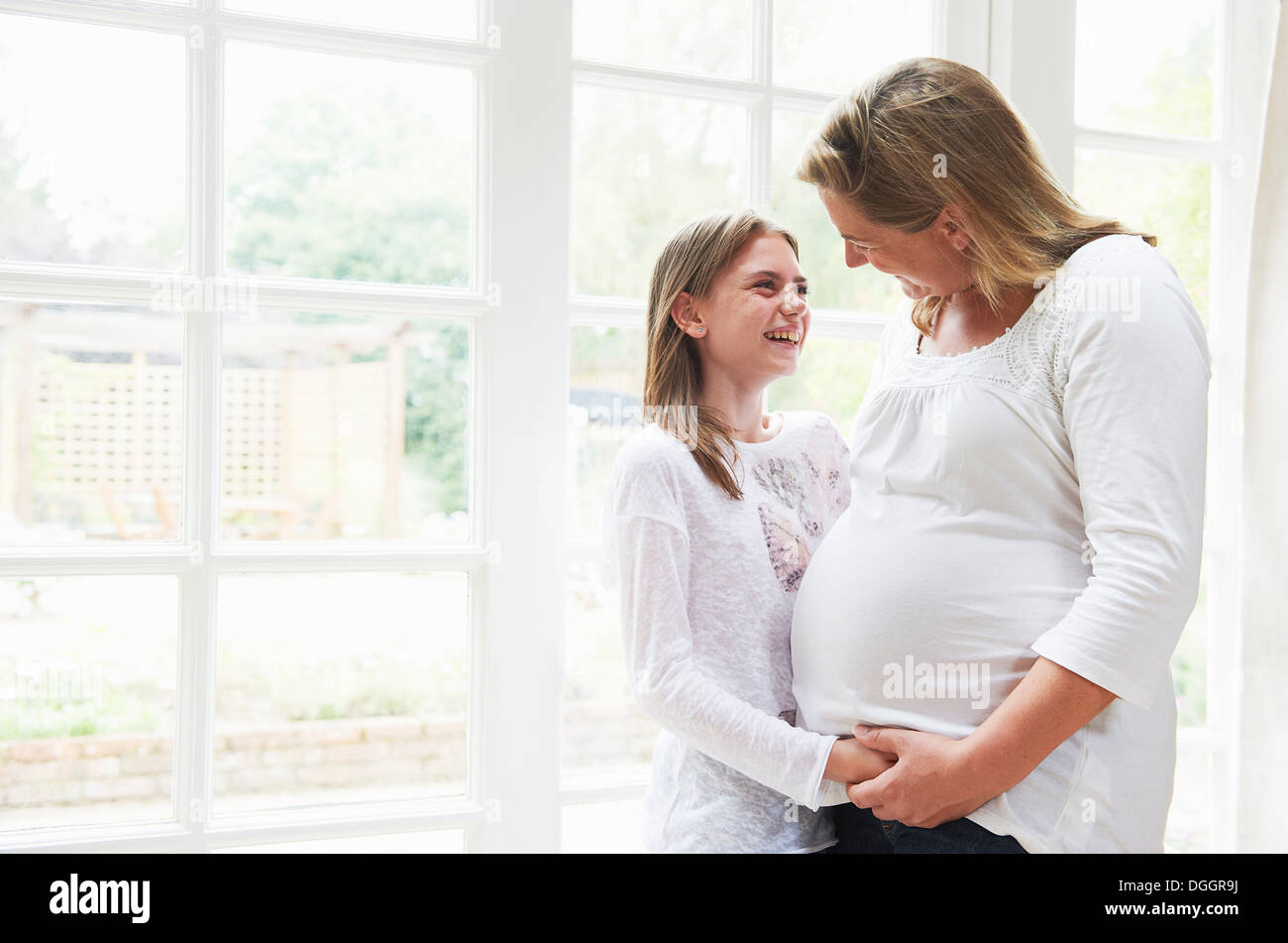 Pregnant mother with teenage daughter by window Stock Photo
