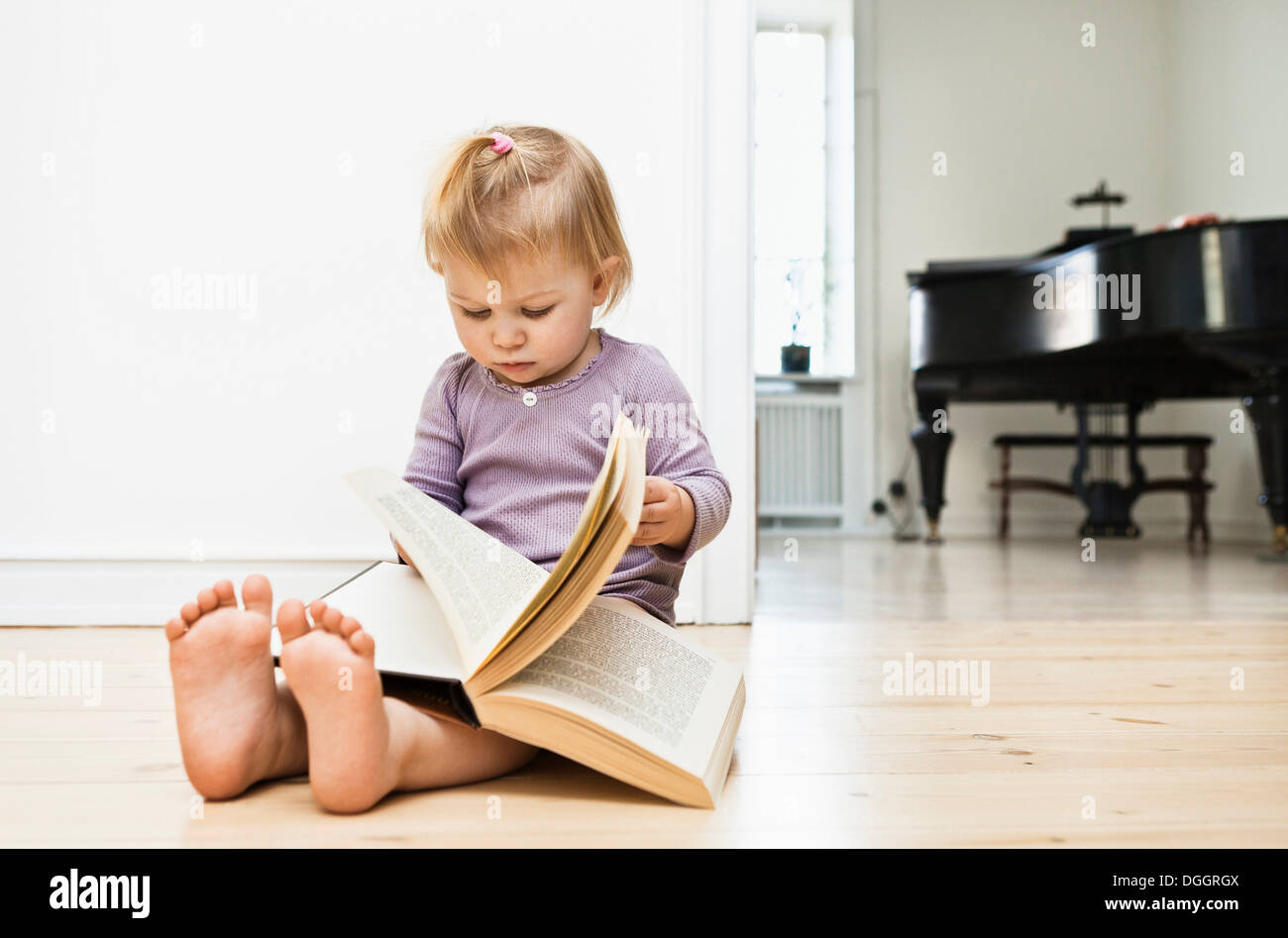 Toddler girl sitting on floor reading book Stock Photo - Alamy