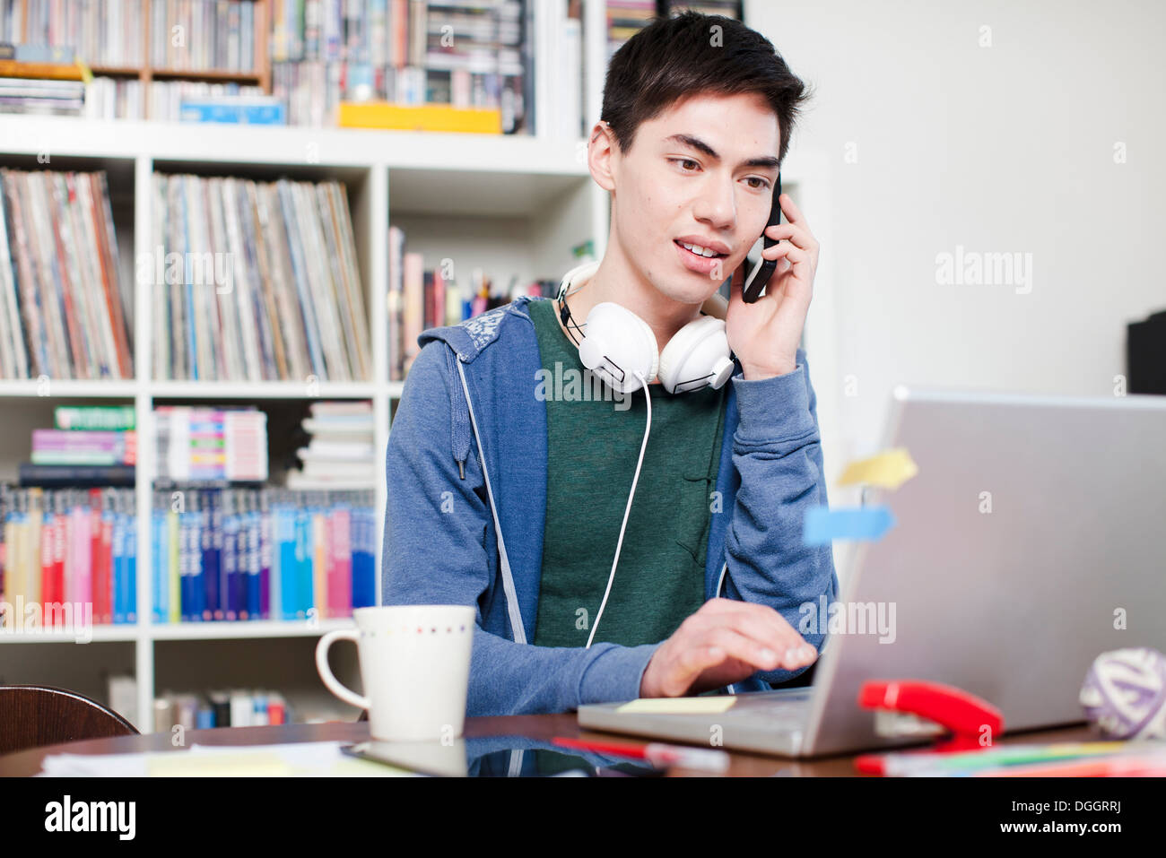 Male student on cell phone using laptop Stock Photo