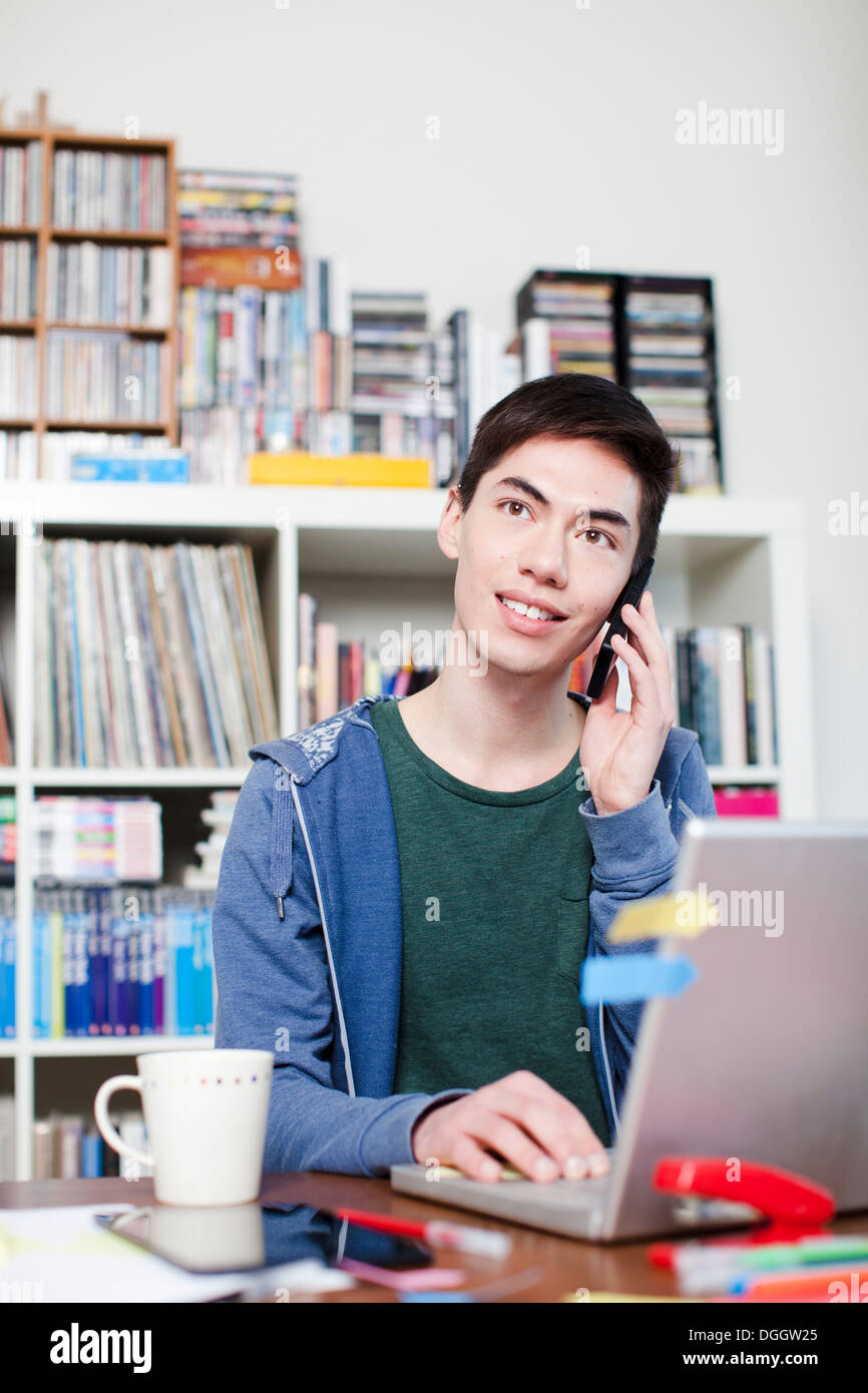 Male student on cell phone using laptop Stock Photo