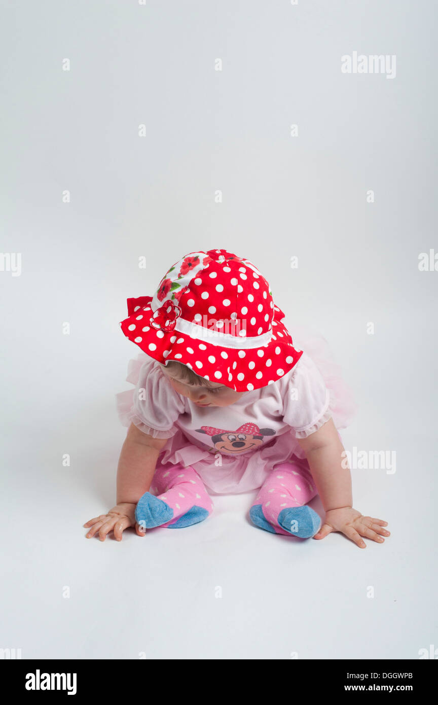 Baby girl sitting on floor in cute pose wearing red polka dot hat Stock Photo