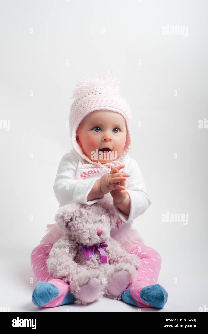 Baby girl with cuddly toy wearing pink woolly hat Stock Photo Alamy