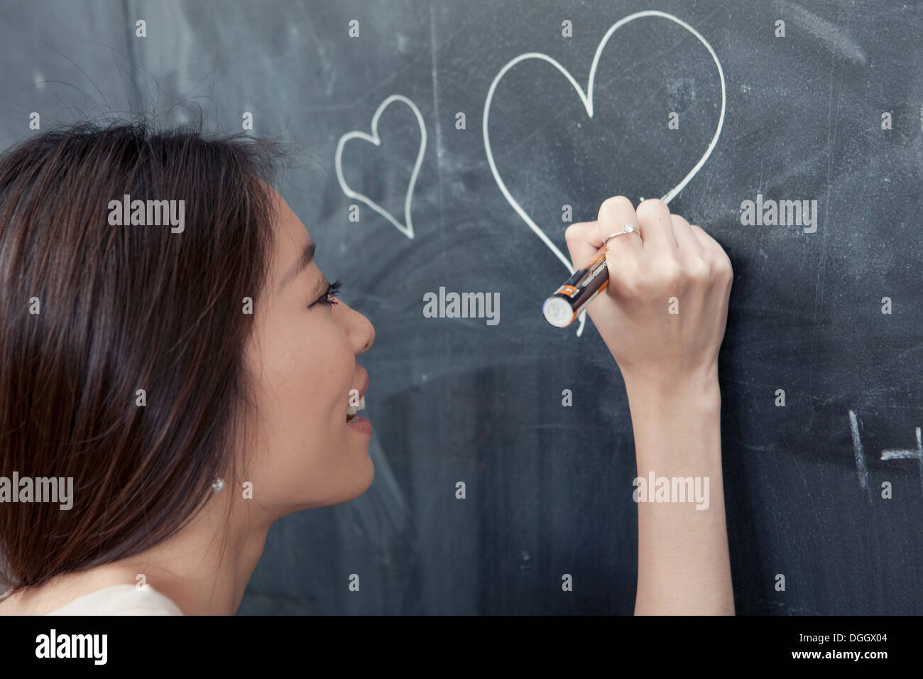 Young woman drawing heart on blackboard Stock Photo
