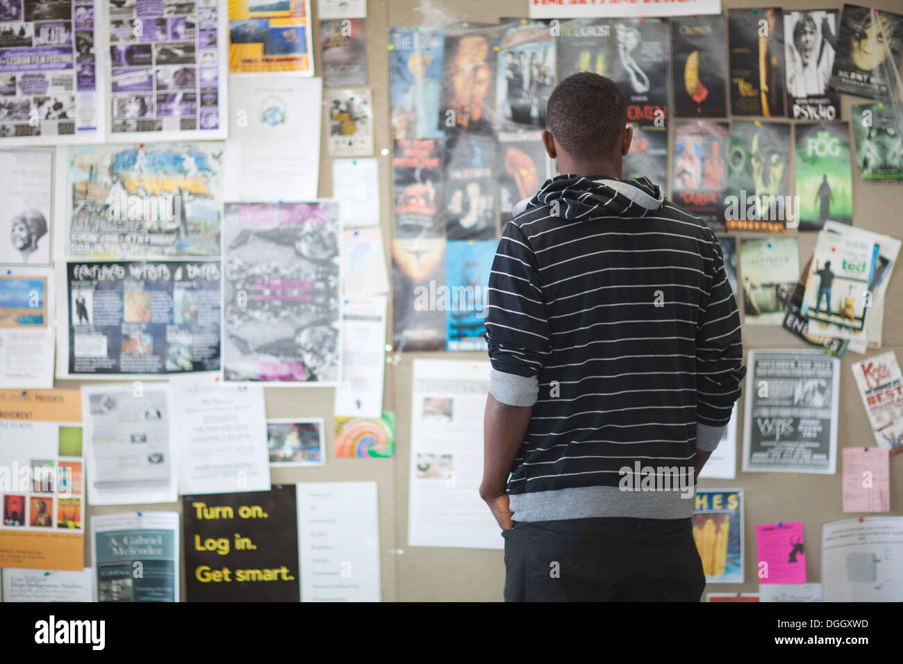 Eighteen year old looks at a bulletin board in college cafeteria filled with job postings, movie listings, event schedule. Stock Photo