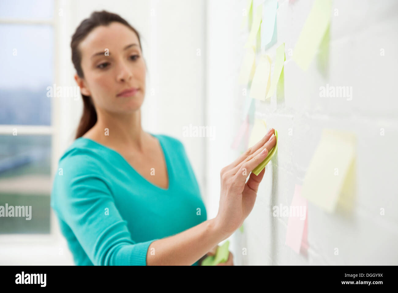 Mid adult woman sticking adhesive notes to wall Stock Photo