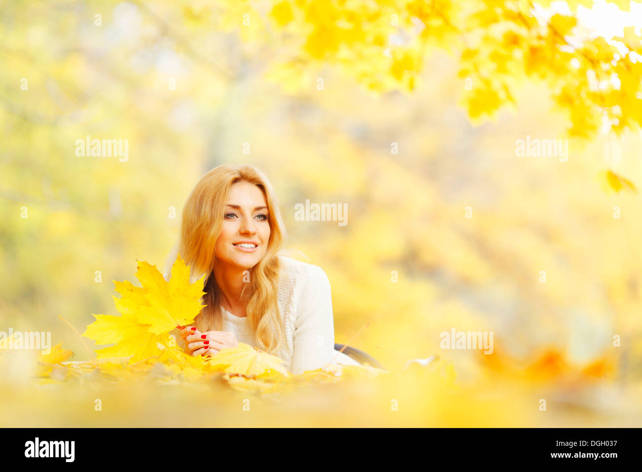 Young woman laying down on the ground covered dry autumnal foliage in beautiful park Stock Photo