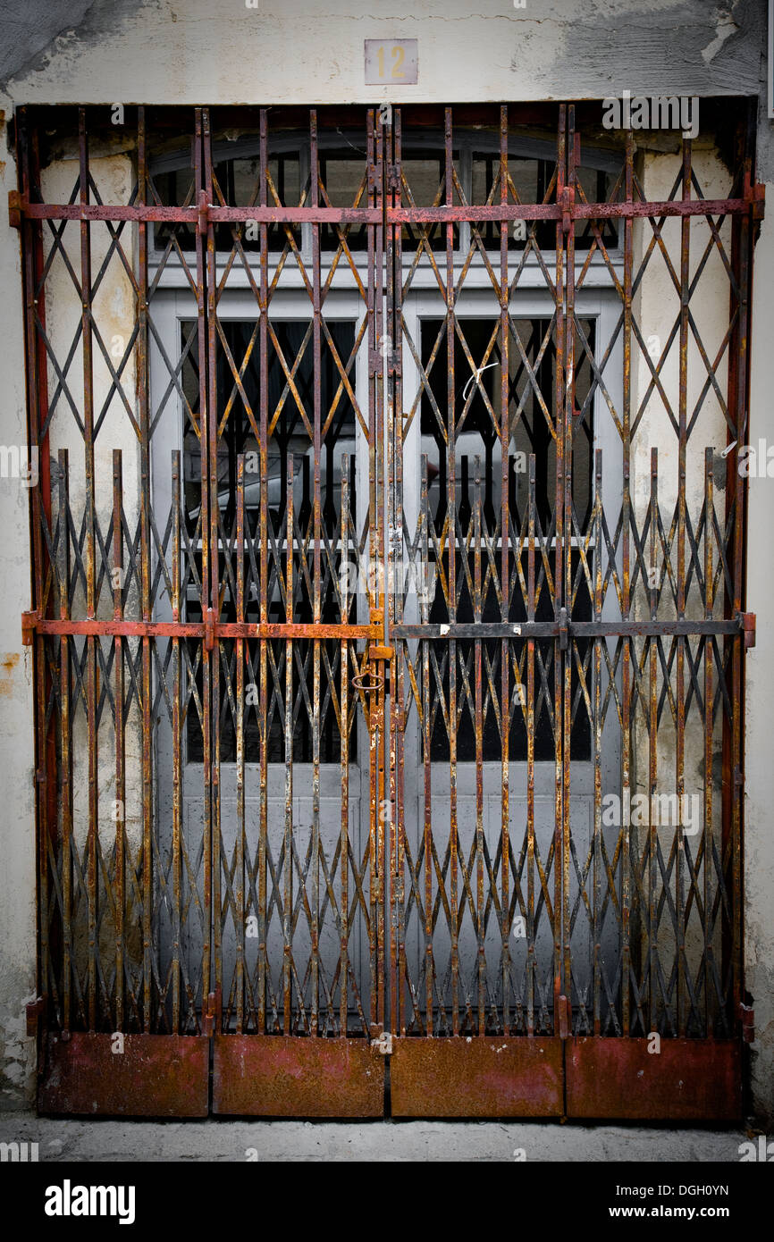 Concertina type rusty metal gates locked in front of a pair of doors