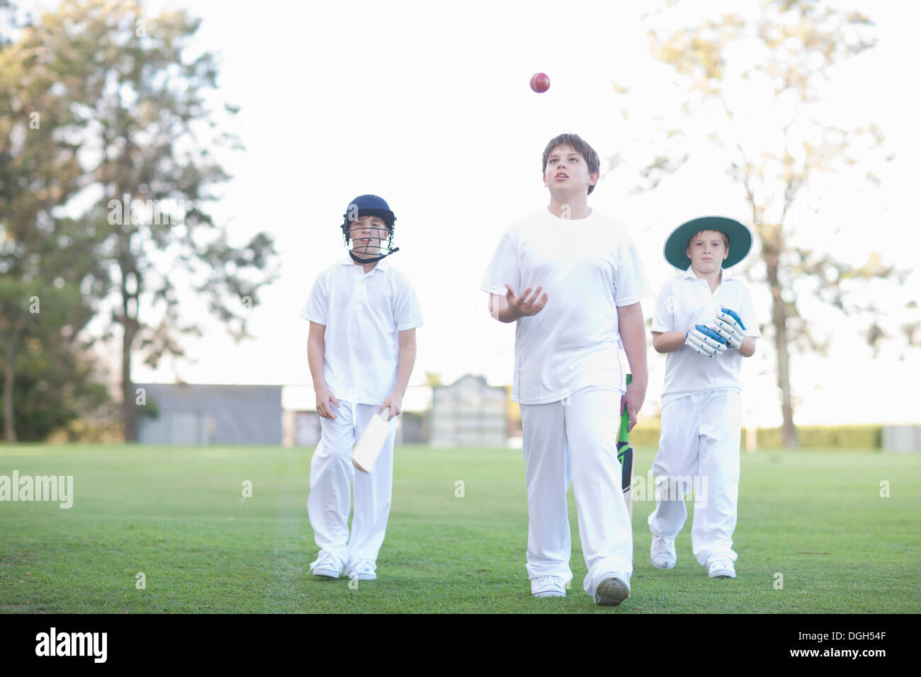Three boys walking on cricket pitch Stock Photo
